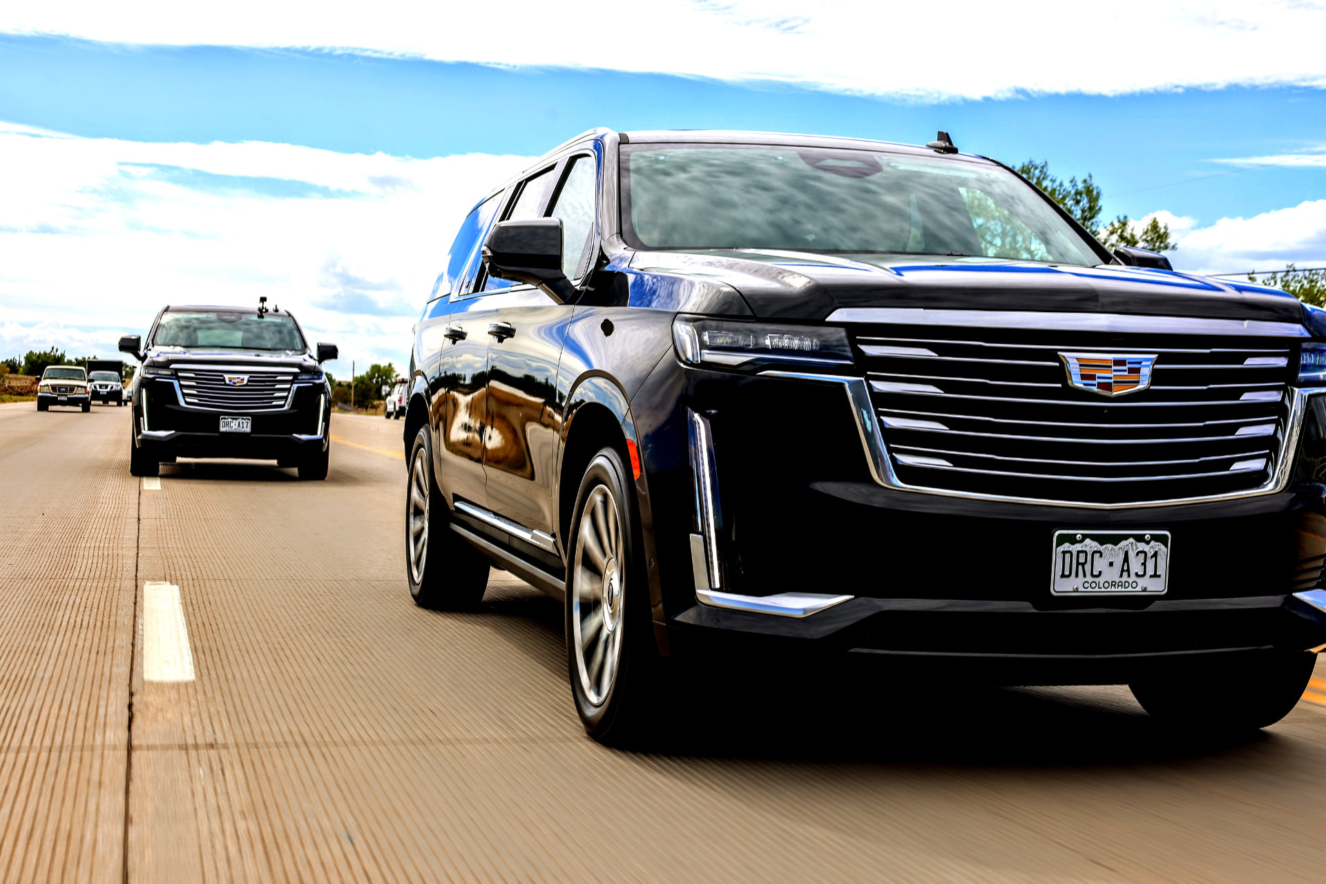 Black executive SUVs traveling together on a roadway.